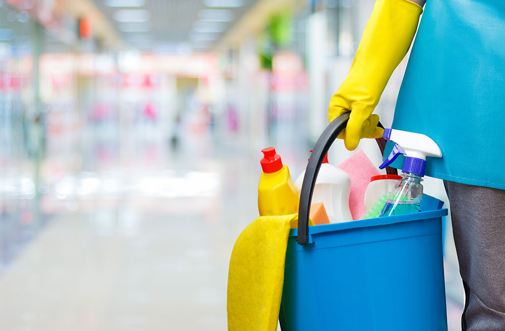 person holding bucket of cleaning supplies in hallway